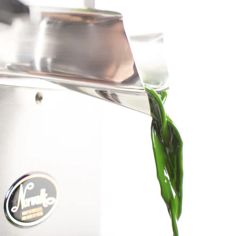 Vibrant green juice flows from a stainless steel cold-press juicer.