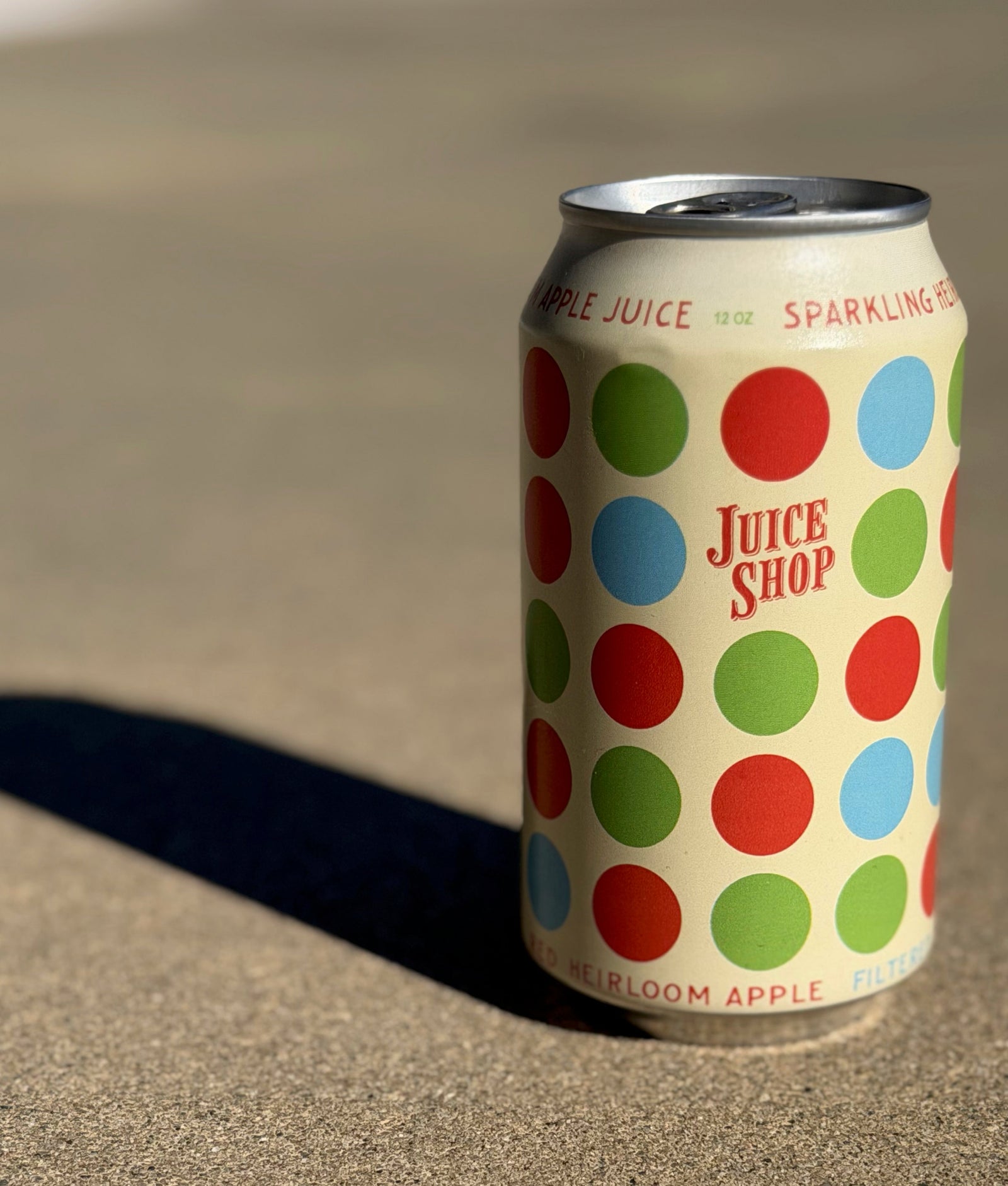 Can with colorful polka dot design and 'Juice Shop' branding on a sandy surface