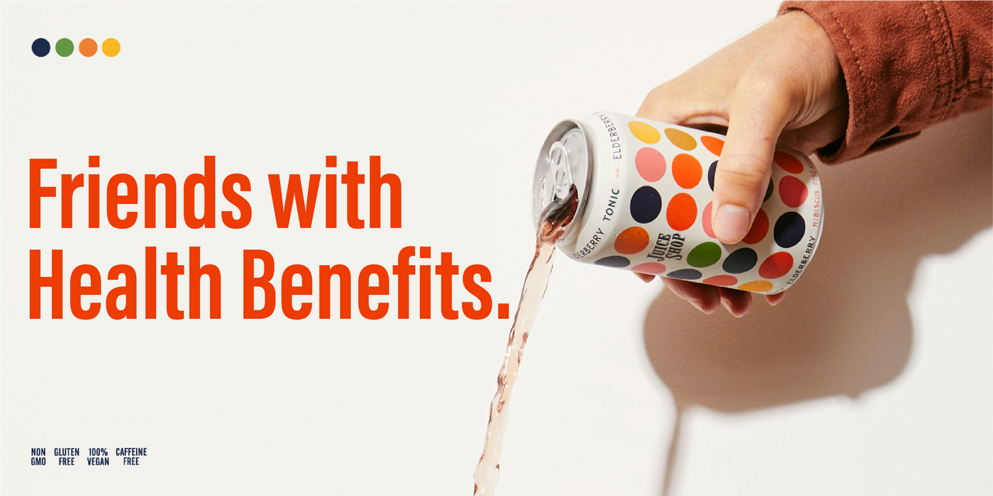 A hand in a rust-colored sleeve tilts a Juice Shop Elderberry Tonic can, pouring a lightly tinted liquid. The can features a vibrant polka-dot design in shades of orange, green, and navy. Bold red-orange text on the left side reads 'Friends with Health Benefits.' Below, small text highlights product benefits: 'Non-GMO, Gluten-Free, 100% Vegan, Caffeine-Free.' The background is a clean, neutral white, emphasizing the product and branding.